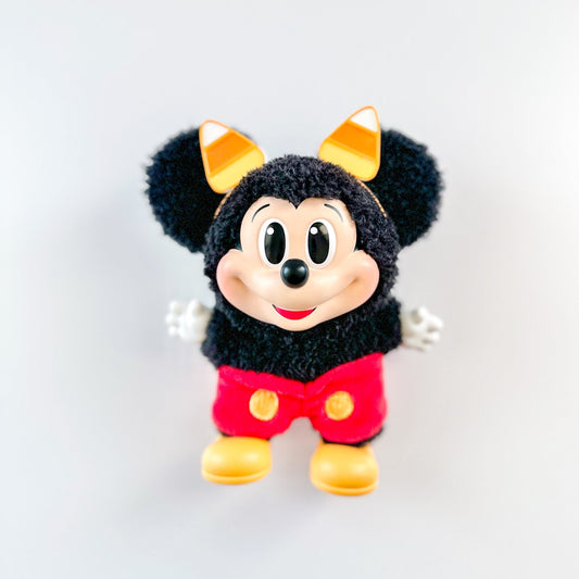 Plush toy resembling a character with black fur, red shorts, and yellow shoes on a white background