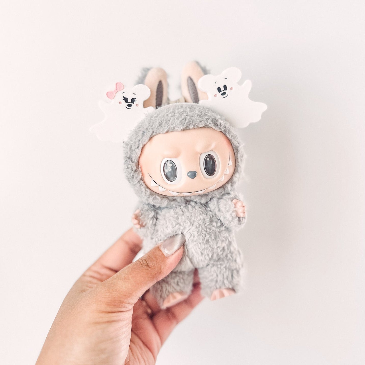 Plush toy resembling a character with bunny ears held by a hand against a white background
