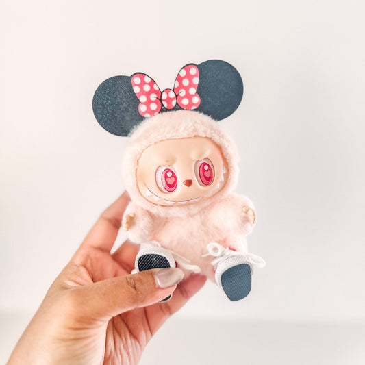 Small plush toy with a bow and ears held by a hand against a light background