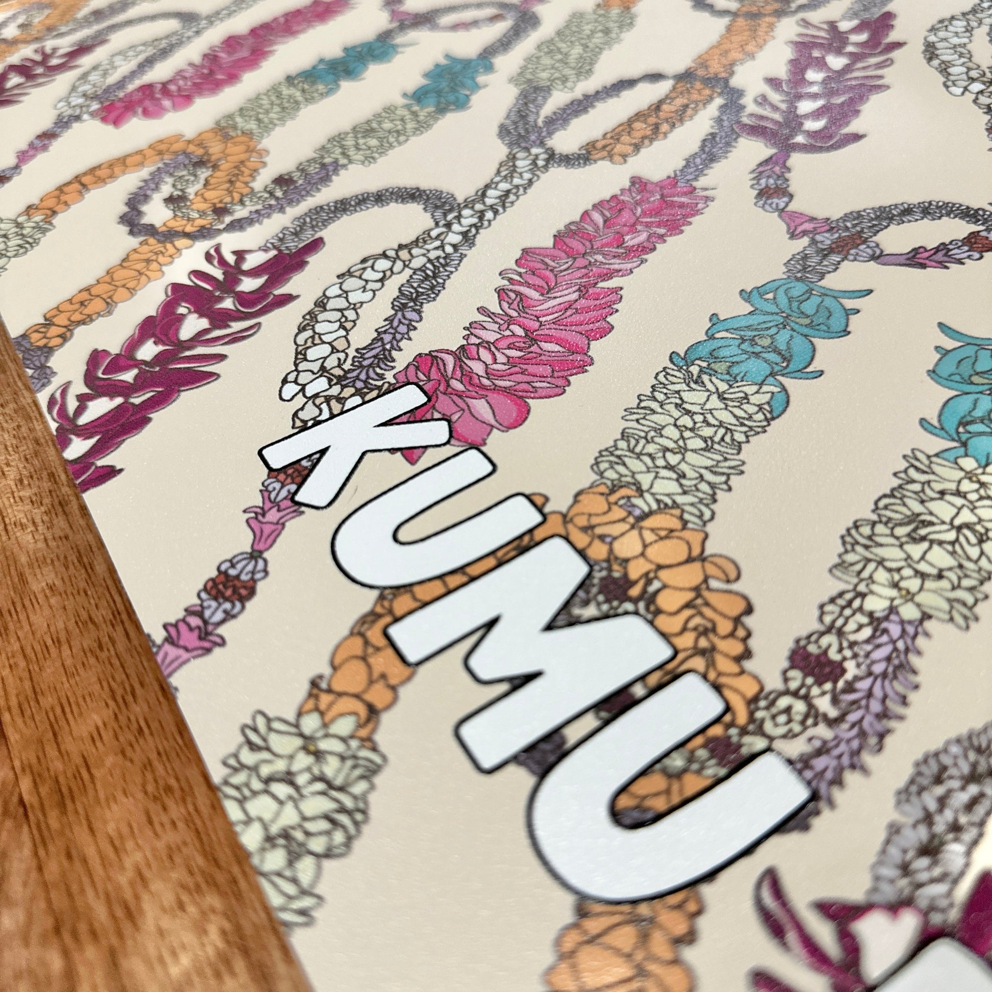 Decorative mat with floral patterns and 'KUMU' branding on a wooden surface.