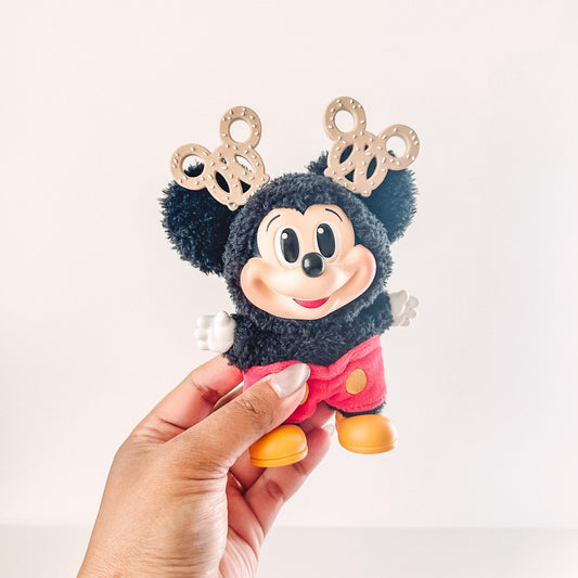Plush toy resembling a character with reindeer antlers held by a hand on a light background