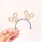 Hand holding a headband with decorative bunny ears on a white background
