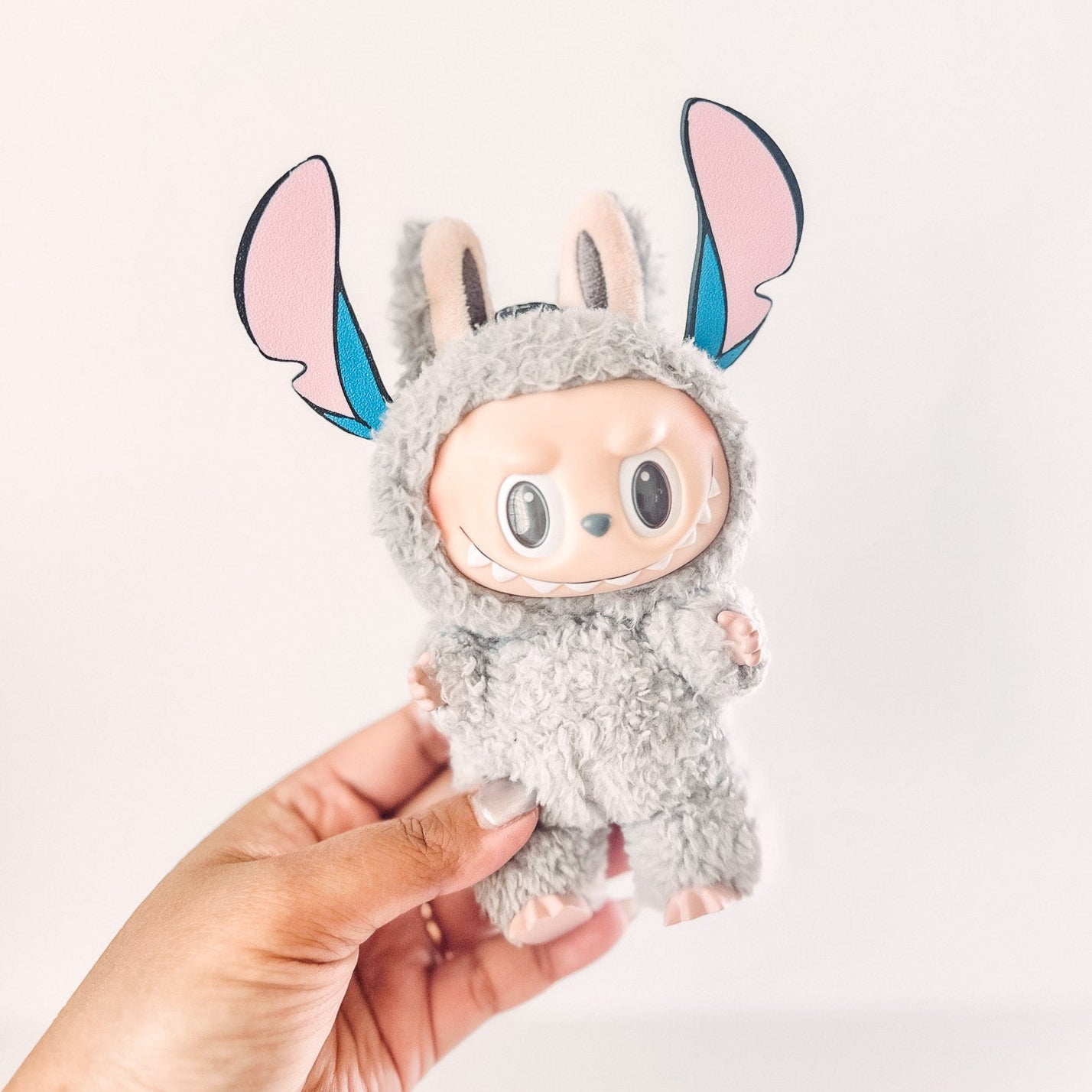 Plush toy resembling a character with large ears held by a hand against a light background